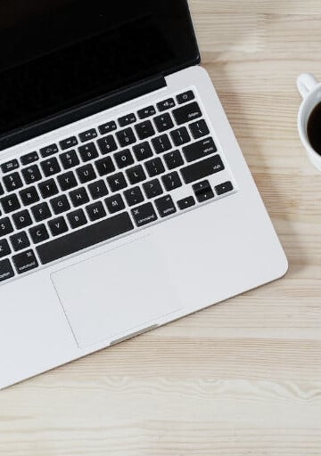 laptop on wooden desk with coffee and pencils