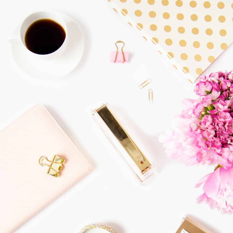 white desktop with coffee, gold stapler and pink notebook