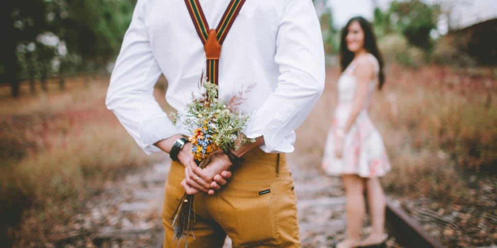 man holding floral bouquet behind back as surprise