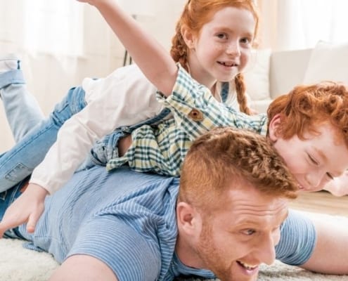 family of father and two kids playing airplanes on the floor, things families do together at home