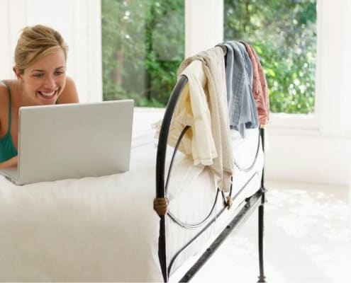 woman in pajamas, on bed, smiling at laptop
