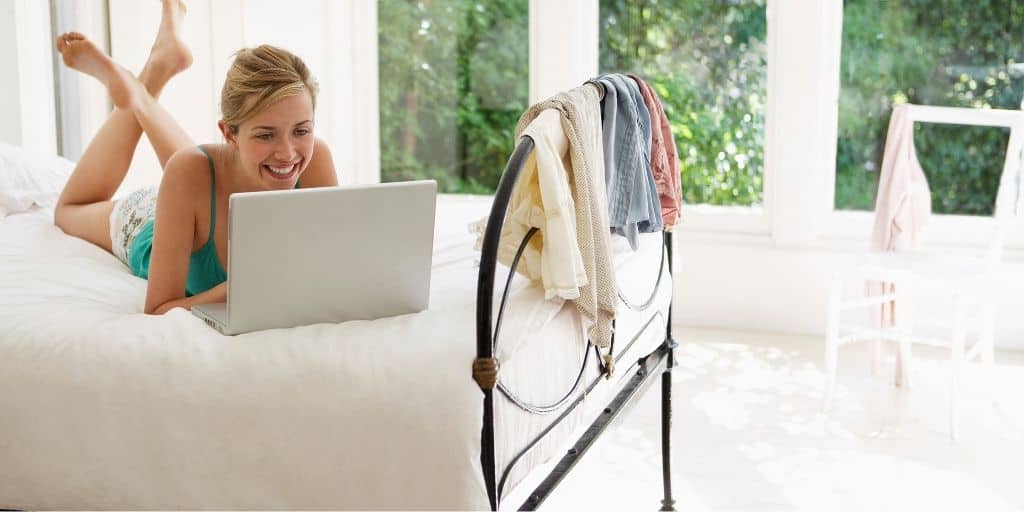 woman in pajamas, on bed, smiling at laptop