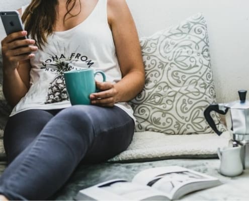woman sitting on bed, reading on phone, with turquoise mug