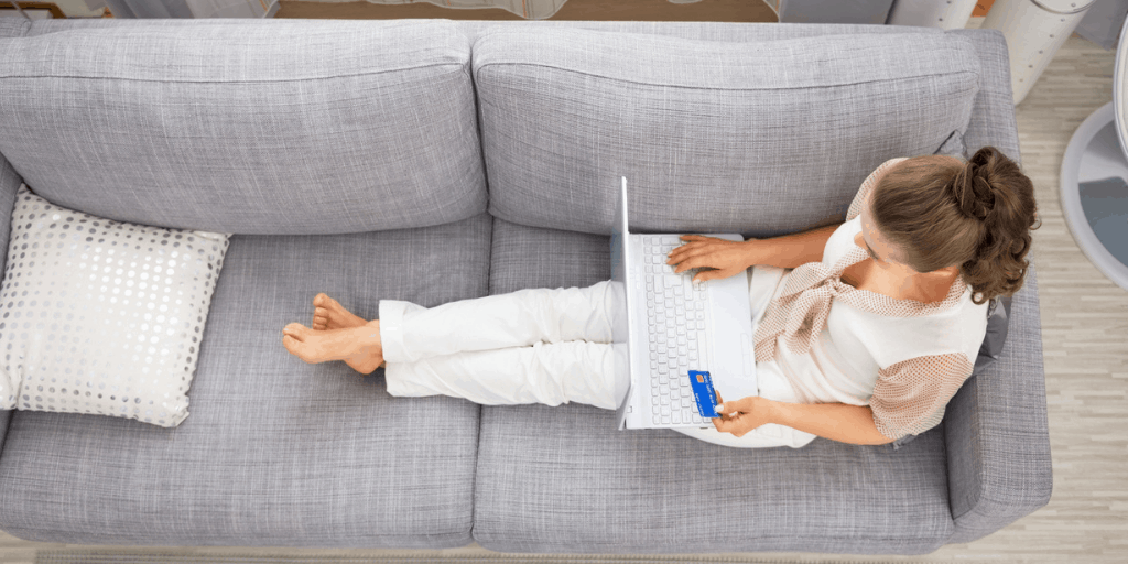 young woman laying on couch with laptop and credit card, wondering how to hide money from herself to stop spending it