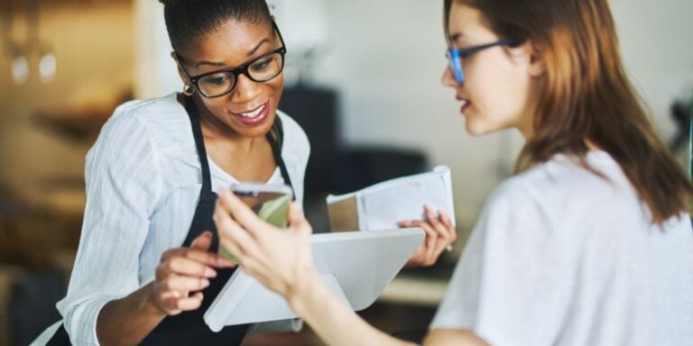 cash register clerk woman reading online coupon from customer on their phone, reading fine print