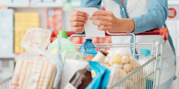 woman holding onto list and coupons at grocery store, with grocery cart, wondering about coupon fraud