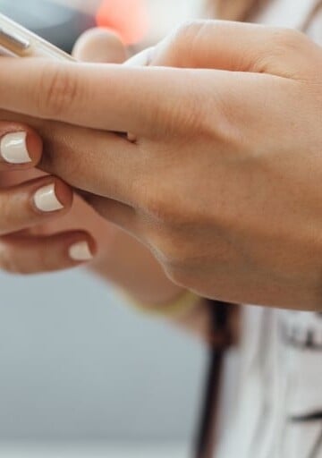 woman with manicured nails holding an iphone, texting