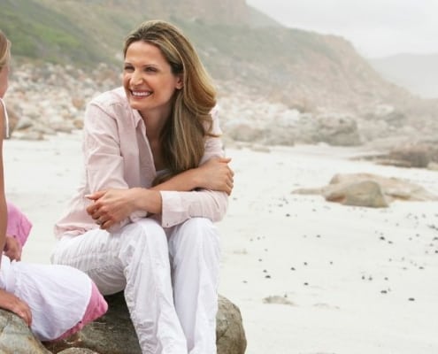 image of mother and daughter on a beach rock, smiling and talking on Mother's Day