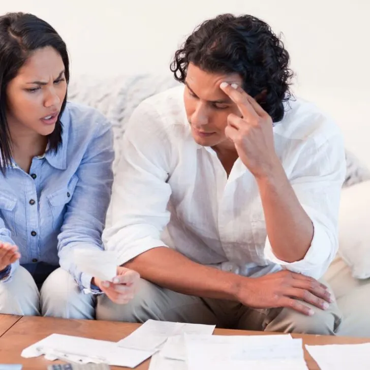 couple on couch looking over finances, woman questioning man