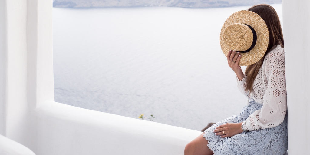 woman sitting on white ledge with hat on her face to cover shame, ocean background