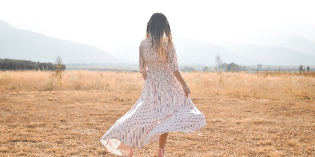 a woman in a white summer dress out in a meadow thinking about money goals