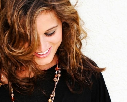 Young woman in black dress, necklace, looking down and smiling