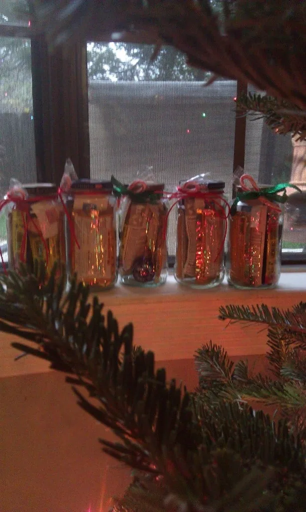 5 empty spaghetti jars on windowsill next to Christmas tree filled with items and wrapped with a candy cane