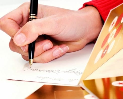 woman's hand writing holiday card messages