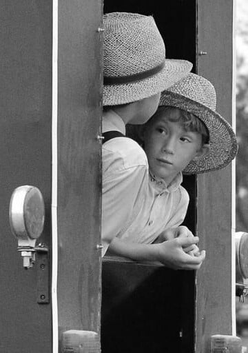 two amish kids hanging out of a horse and buggy, talking, black and white photo