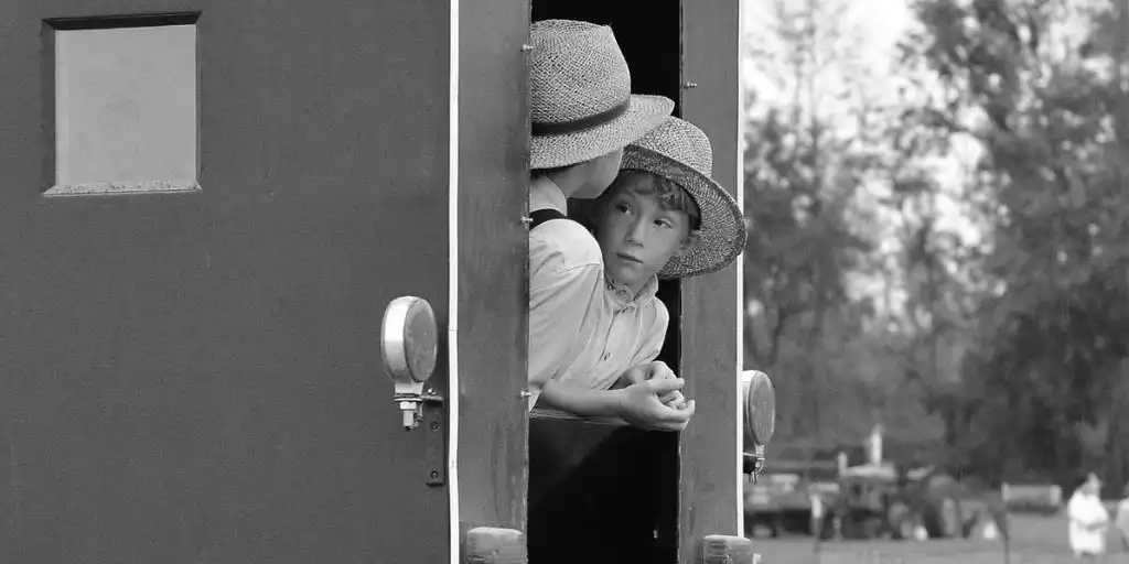 two amish kids hanging out of a horse and buggy, talking, black and white photo