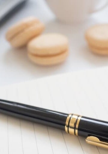 a desk with pen, pad of paper, laptop, and macaroons