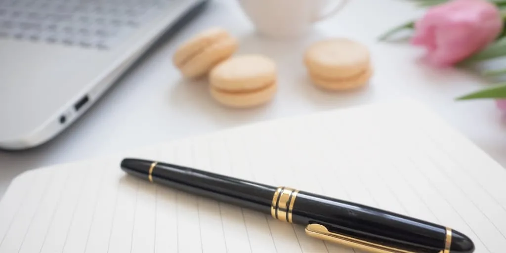 a desk with pen, pad of paper, laptop, and macaroons