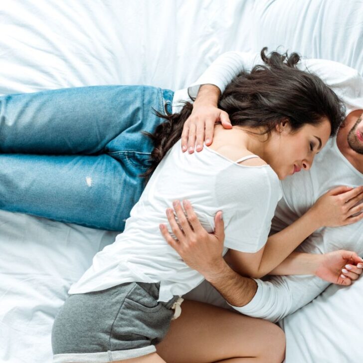couple in blue jeans and shorts in bed, woman's head on man's chest