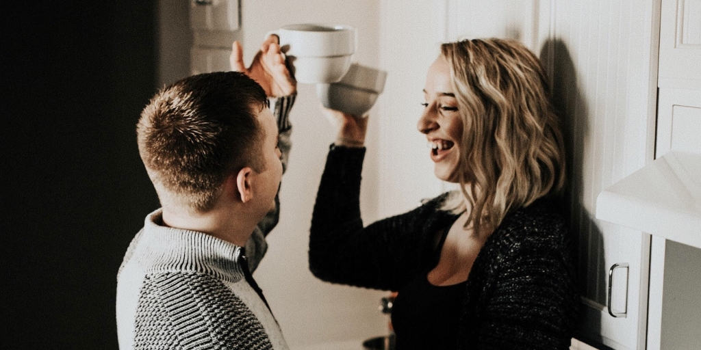 couple in kitchen, woman on counter, toasting each other smiling