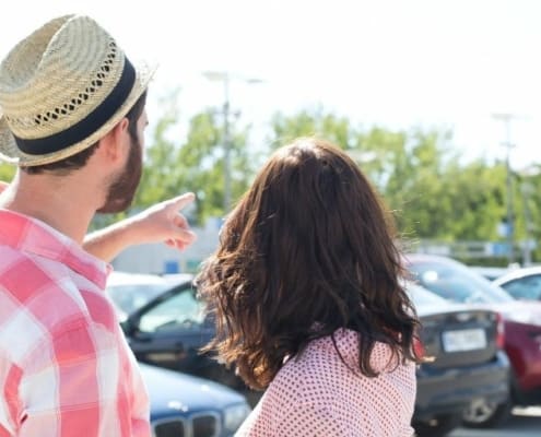 young couple in rental car parking lot, pointing to a car