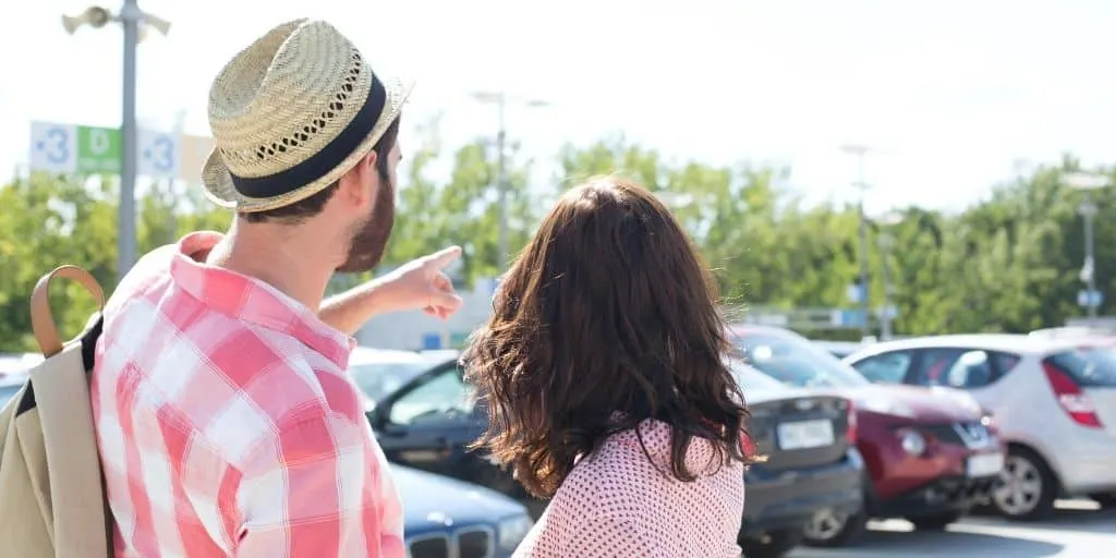 young couple in rental car parking lot, pointing to a car