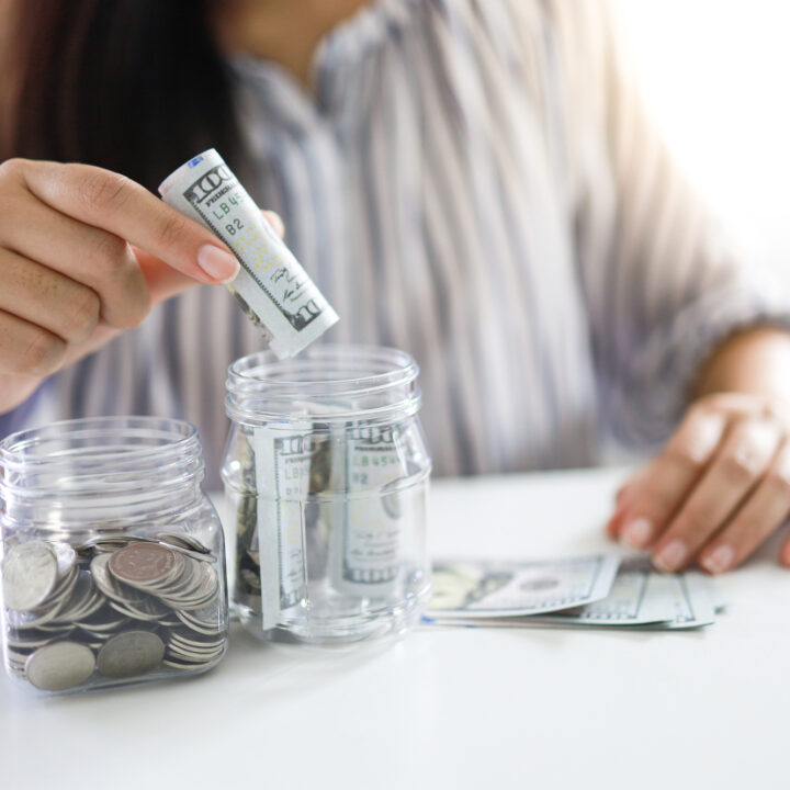 woman's hands putting money into two savings jars for multiple savings goals