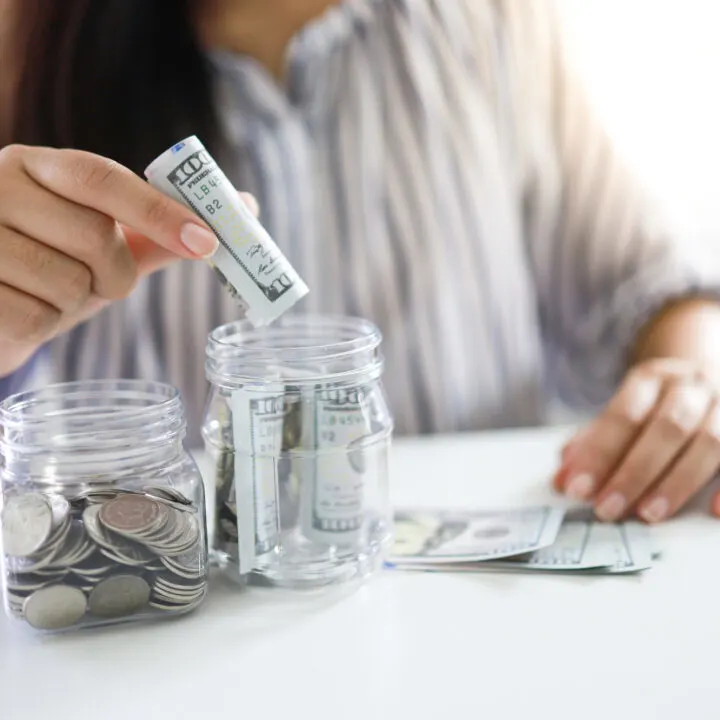 woman's hands putting money into two savings jars for multiple savings goals