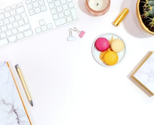 white desk, white keyboard, colorful macaroons, plant, notepad