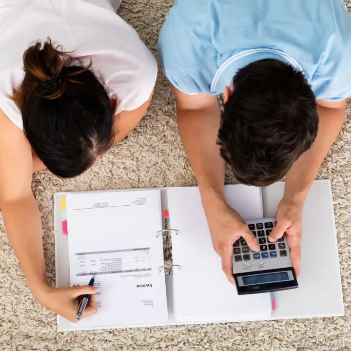 looking down on young couple with calculator, working on how to pay off debt and save money at the same time
