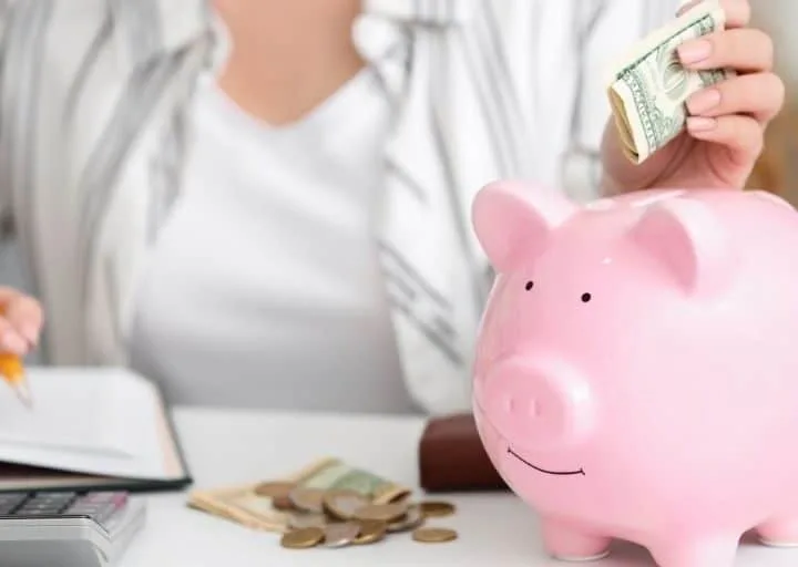 woman in striped shirt putting money into piggy bank at desk