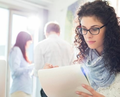 young woman in glasses, writing down life lessons about money on notebook