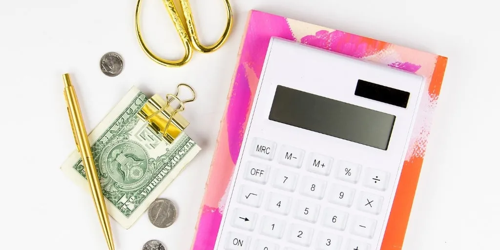 white desktop with pink notepad and calculator, money in clip