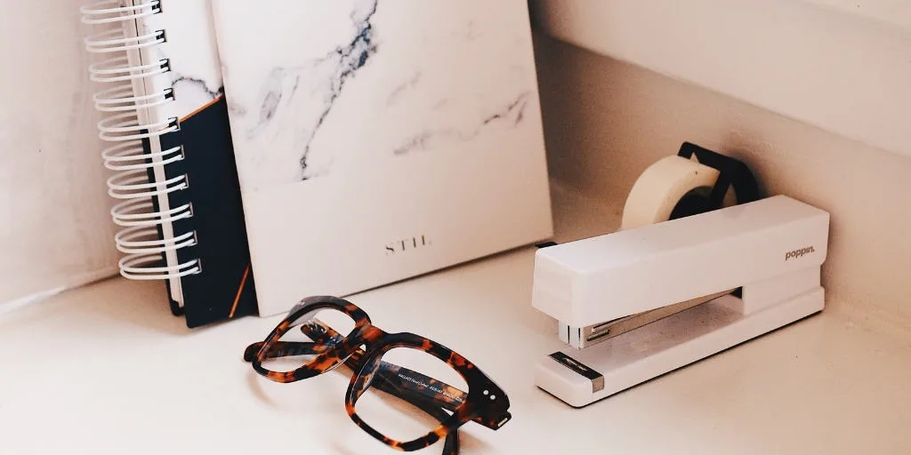 pink marble desktop with glasses, books, and stapler