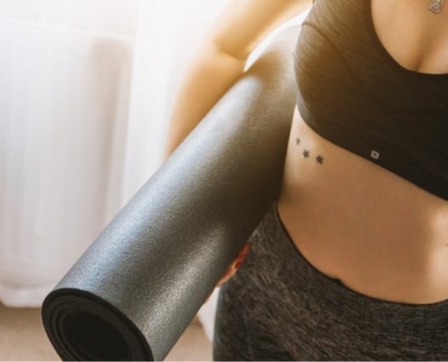 young woman in gym outfit, holding yoga mat, at gym