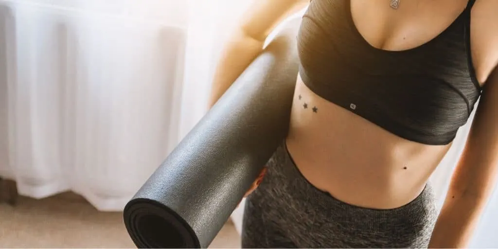 young woman in gym outfit, holding yoga mat, at gym