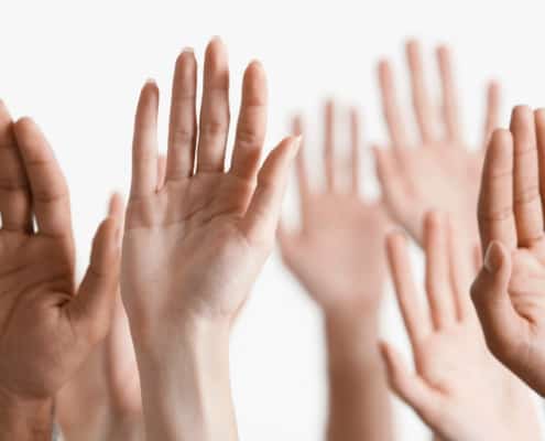 group of hands of all nationalities raised to volunteer, on white background