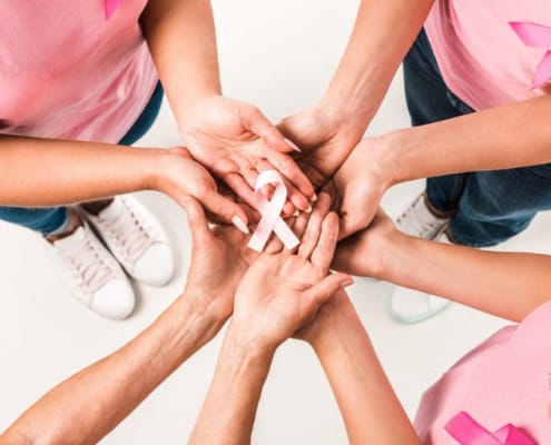 a group of females wearing pink shirts holding a pink cancer ribbon together