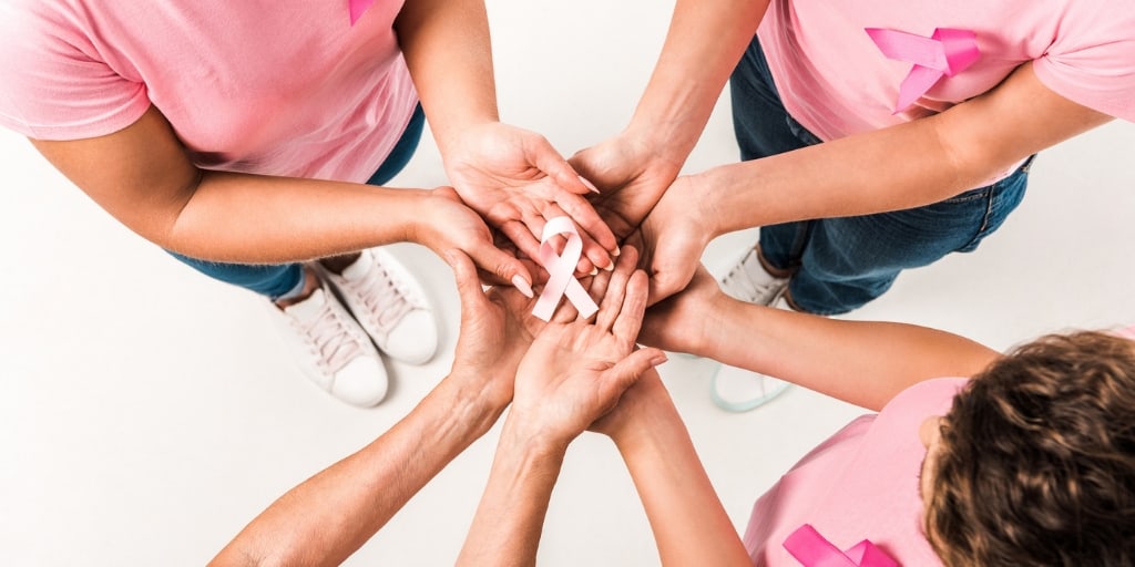 a group of females wearing pink shirts holding a pink cancer ribbon together