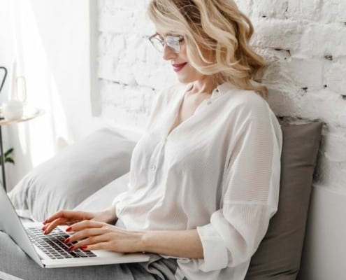 adult woman on laptop, smiling, in bed, volunteering from home