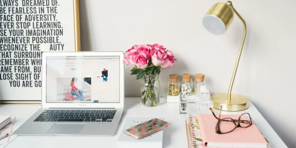 white desk with laptop, gold lamp, pink flowers