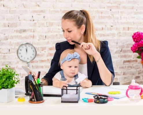 young woman with baby in lap working from home at desk