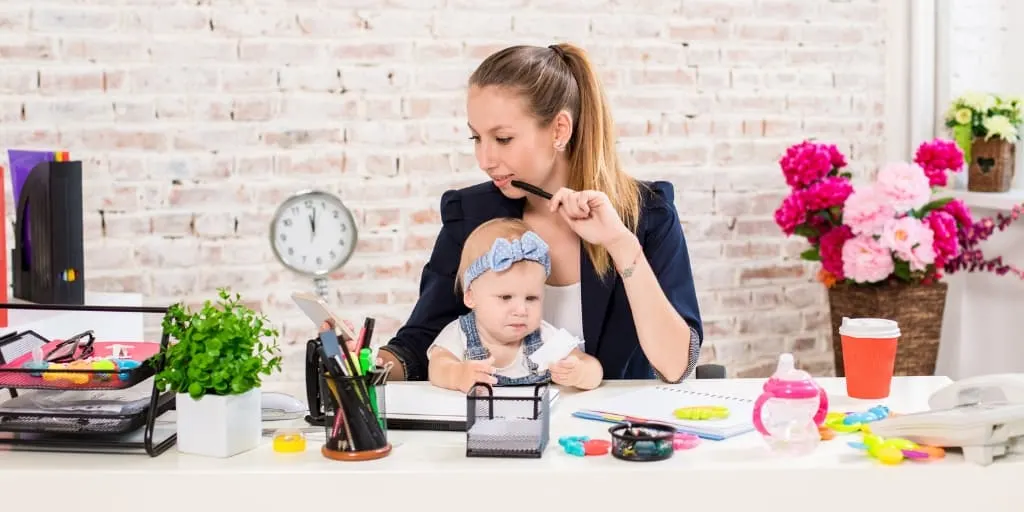 young woman with baby in lap working from home at desk