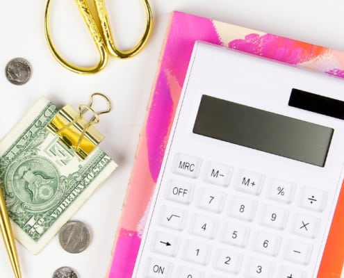 white desktop with calculator, money in clip, gold scissors