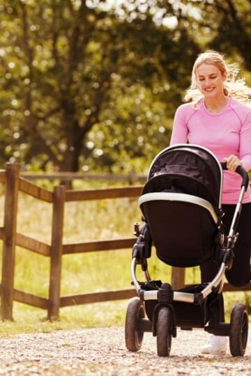 woman in pink shirt smiling into stroller, walking with fitbit