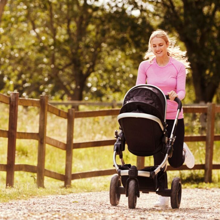 woman in pink shirt smiling into stroller, walking with fitbit