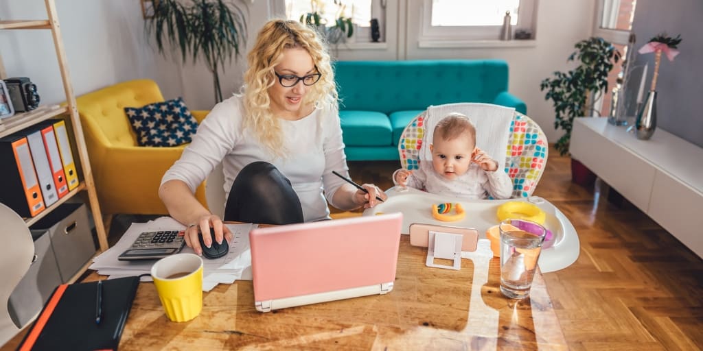 woman with glasses working on laptop at kitchen table with baby