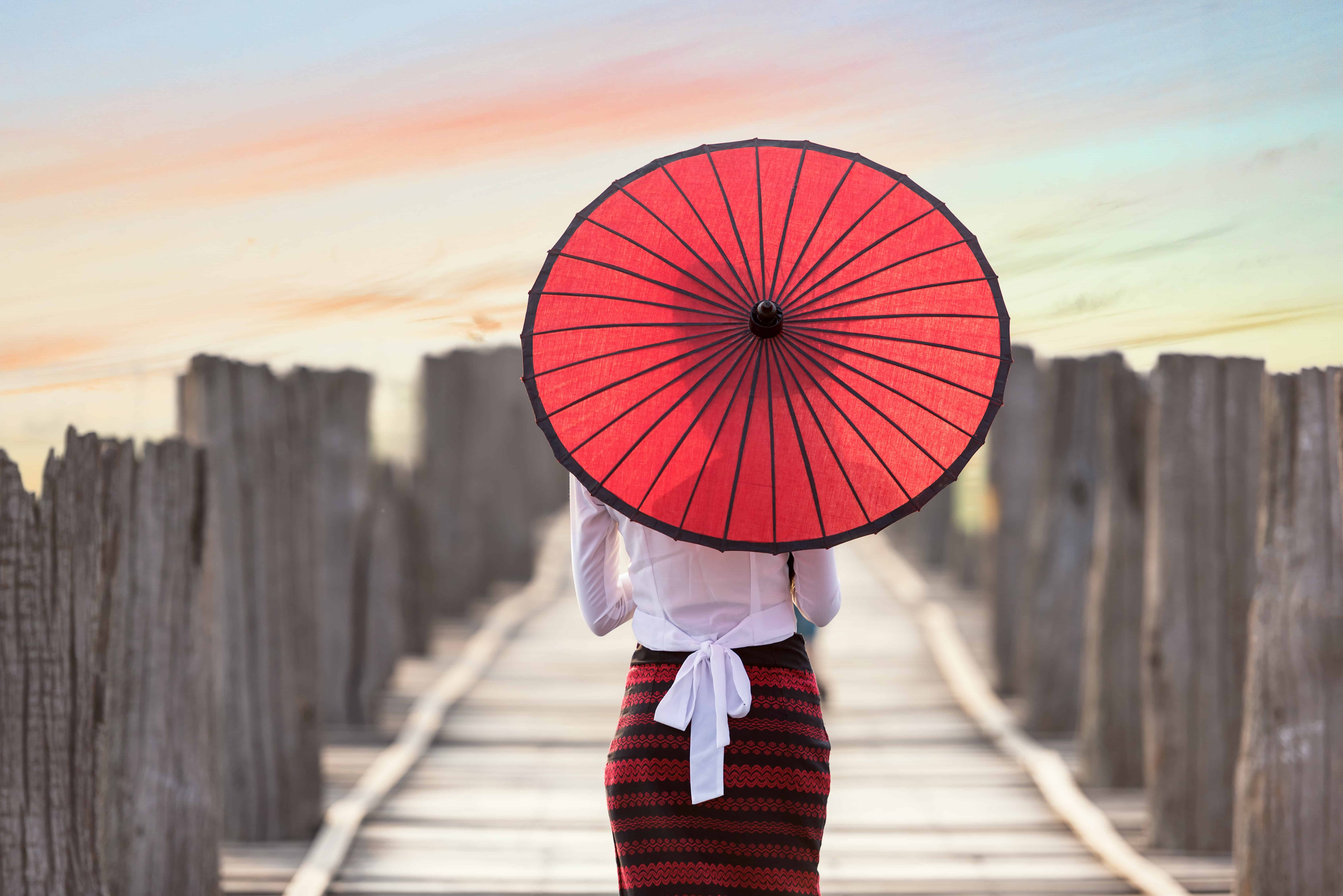 woman with pencil skirt and red Asian umbrella walking down dock