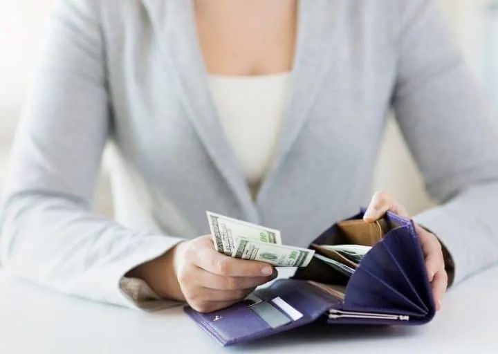 woman in light blue blazer, pulling cash out of navy blue wallet to avoid common budget pitfalls