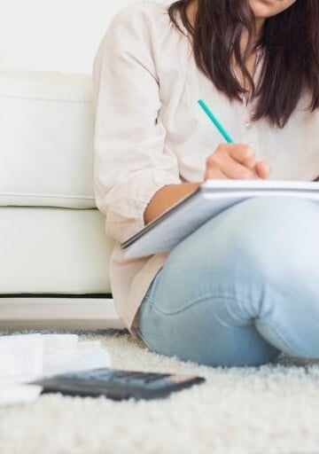 woman in jeans on floor, writing in notepad with a calculator
